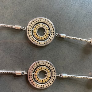 May include: A silver necklace with two round pendants. Each pendant has a concentric circle design with a gold center.