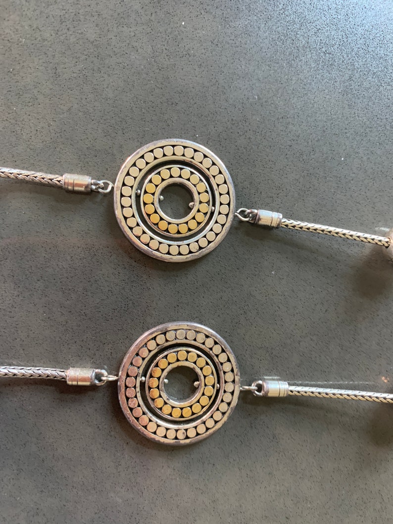 May include: A silver necklace with two round pendants. Each pendant has a concentric circle design with a gold center.
