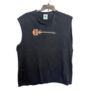 Puede incluir: Camiseta negra sin mangas con un gr&aacute;fico de guitarra. La guitarra tiene un cuerpo colorido y un m&aacute;stil plateado. La camiseta est&aacute; colgada en una percha negra sobre un fondo blanco.