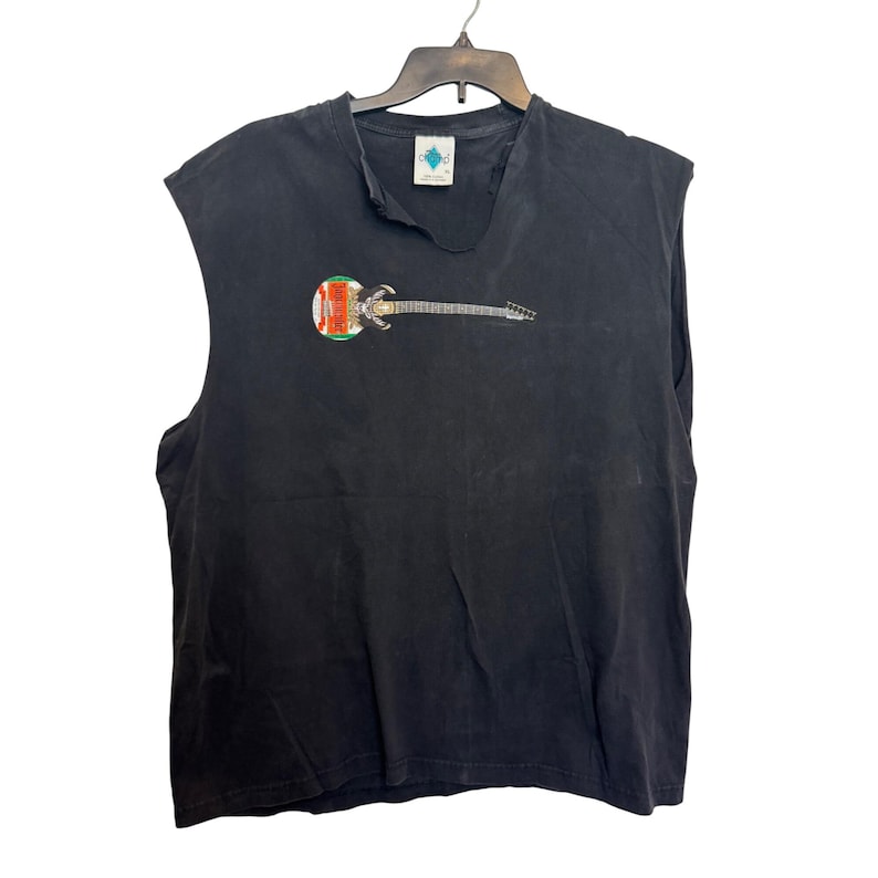 Puede incluir: Camiseta negra sin mangas con un gr&aacute;fico de guitarra. La guitarra tiene un cuerpo colorido y un m&aacute;stil plateado. La camiseta est&aacute; colgada en una percha negra sobre un fondo blanco.