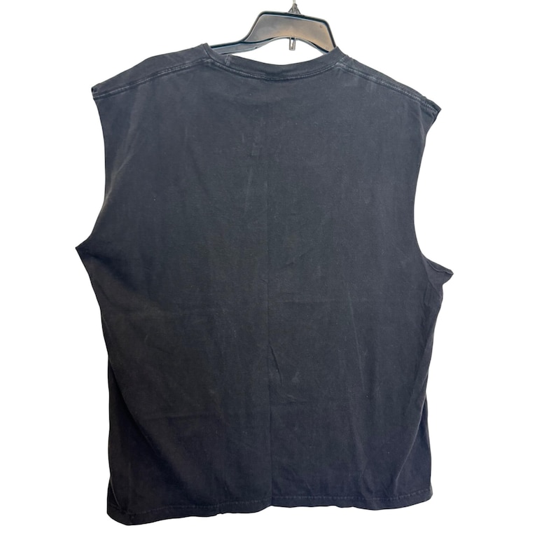 Puede incluir: Una camiseta negra sin mangas colgada de una percha negra. La camiseta est&aacute; hecha de una tela suave y oscura. La camiseta se ve desde atr&aacute;s.