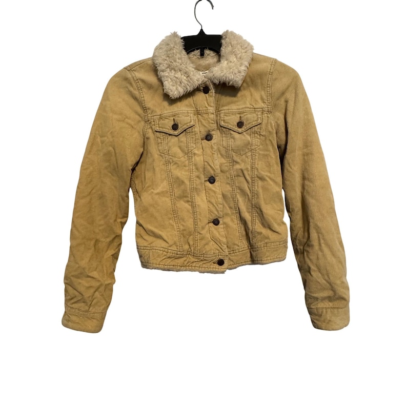 May include: A tan corduroy jacket with a cream-colored faux fur collar. The jacket has a button-up front, two chest pockets, and two side pockets. The jacket is hanging on a black hanger.