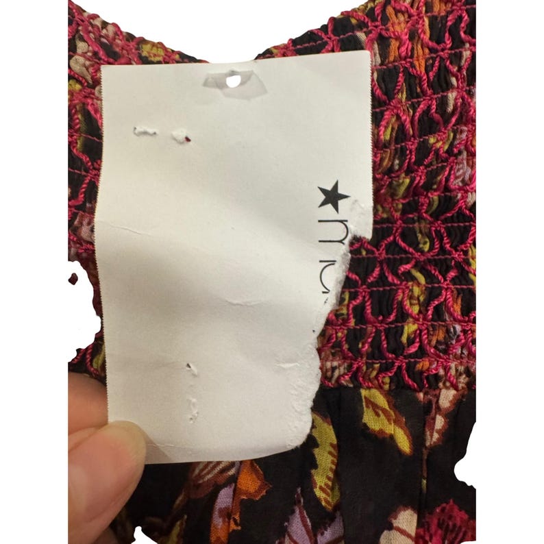 May include: Close-up of a floral print dress with a tag. The dress has a black background with colourful floral patterns. The top of the dress has a pink, textured design. The tag is white with a partially visible logo.