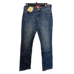 May include: Blue denim jeans with a straight leg cut, hanging on a black hanger. The jeans have a faded wash and a small amount of distressing. A Lucky Brand tag is attached to the front pocket.