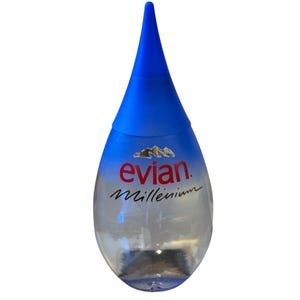 Könnte beinhalten: Eine klare, tropfenförmige Evian-Wasserflasche mit blauem Verschluss. Die Flasche hat das Evian-Logo in Rot und das Wort "Millennium" in Schreibschrift. Der Verschluss ist leuchtend blau, der Flaschenkörper transparent.