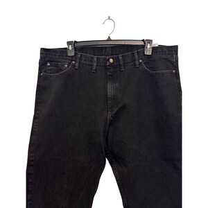 Op de afbeelding: Zwarte denim jeans hangend aan een zwarte hanger. De jeans hebben een klassiek ontwerp met vijf zakken met een knoop- en ritssluiting. De denim lijkt een donkere wassing te hebben, met een lichte glans.