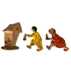 May include: Three ceramic figurines. A tan outhouse with a thatched roof and flowers. A person in a yellow robe carrying a lantern. A person in a red robe carrying a bottle. All are on a white background.