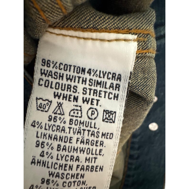 May include: A white care label with black text and symbols. The text reads "96% Cotton 4% Lycra Wash with similar colours. Stretch when wet. 96% Bomull, 4% Lycra. Tvattas med liknande f&auml;rger. 96% Baumwolle, 4% Lycra. Mit &auml;hnlichen Farben Waschen 96% Coton, 4%"