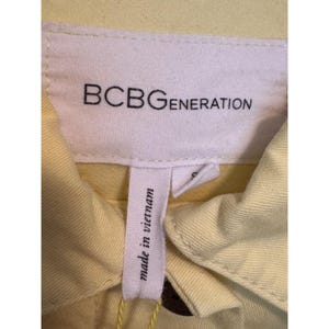 May include: A close-up shot of a pale yellow garment tag. The white tag displays "BCBGGENERATION" in black. Beneath it, a smaller tag reads "made in vietnam". The garment itself is a light yellow hue.