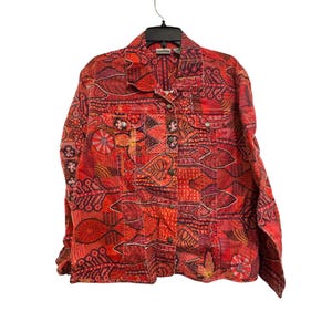 May include: A red, orange, and burgundy patterned jacket with a button-up front and two chest pockets. The jacket features an intricate design with floral and geometric shapes. The jacket is hanging on a black hanger.