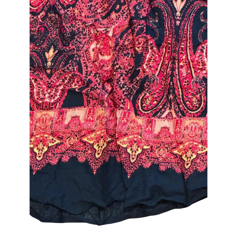 May include: Close-up of a fabric with a paisley pattern in shades of red, pink, and navy blue. The fabric features intricate floral and teardrop designs, with a decorative border at the bottom.
