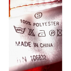 May include: White fabric tag with black text that reads "100% POLYESTER", "MADE IN CHINA", and "S/N 106822". The tag also includes care instructions with symbols for machine wash, tumble dry, iron, and do not dry clean.