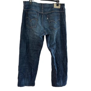 May include: Dark wash denim jeans with classic five-pocket styling. The jeans feature the Levi's brand logo on the back pockets and a small tag on the back waistband. The jeans are hanging on a black hanger.