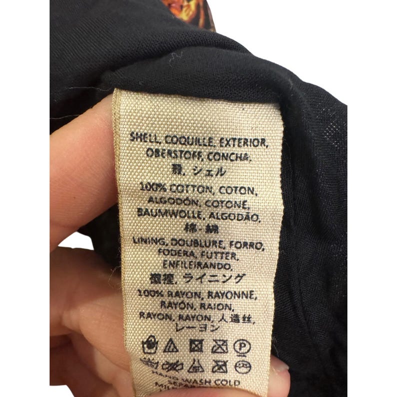 May include: A clothing label with text in multiple languages, including English, French, German, Spanish, Italian, and Portuguese. The label details the fabric composition, listing 100% cotton and 100% rayon. Washing instructions are also visible.