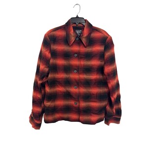 May include: A long-sleeve button-up shirt featuring a red and black plaid pattern. The shirt has a pointed collar, a front button closure with dark buttons, and is displayed on a black plastic hanger. The interior label reads Crossing Points.