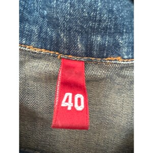 May include: A close-up of a red size tag with the number 40 printed in white on a blue denim jacket.