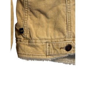 May include: Close-up of a tan corduroy jacket with a button closure and a white, fuzzy lining. The jacket has a small A&F label. The corduroy fabric has vertical ridges.