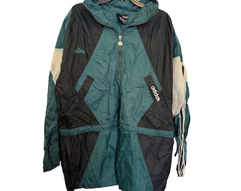 May include: Vintage Adidas anorak jacket in teal, black, and white. The jacket features a half-zip closure, a hood, and the Adidas logo on the sleeve. The design includes geometric color-blocking and a drawstring waist. The jacket is hanging on a black hanger.