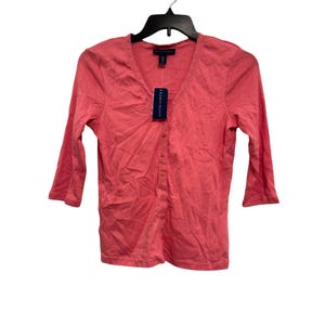May include: A coral pink button-down cardigan with three-quarter length sleeves and a V-neckline featuring delicate lace trim. The garment includes a vertical row of matching buttons and a Karen Scott brand tag attached to the collar area.
