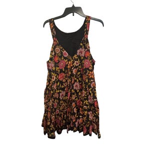 May include: A black sleeveless dress with a V-neck and a floral design. The dress has pink, orange, and yellow flowers. It is hanging on a black hanger.