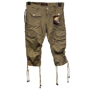 May include: Olive green capri pants with multiple pockets and decorative metal buttons. The pants have drawstring details at the knees and a tag that reads "GREAT".