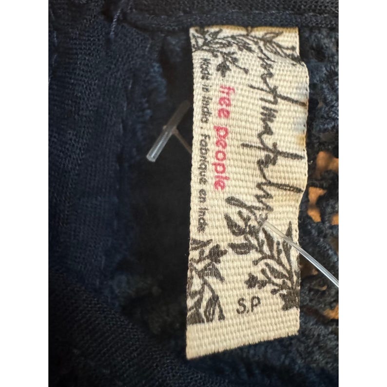 May include: Close-up of a navy blue garment with a Free People label attached. The label is cream-colored with the brand name in a stylized font and the text "Made in India, Fabriqu&eacute; en Inde". The size is S.P.