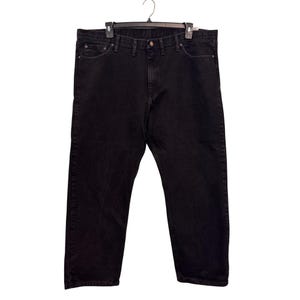 Op de afbeelding: Zwarte denim jeans hangend aan een zwarte hanger. De jeans hebben een klassiek ontwerp met vijf zakken met een knoop- en ritssluiting. De jeans zijn effen zwart.