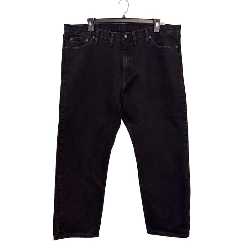 Op de afbeelding: Zwarte denim jeans hangend aan een zwarte hanger. De jeans hebben een klassiek ontwerp met vijf zakken met een knoop- en ritssluiting. De jeans zijn effen zwart.