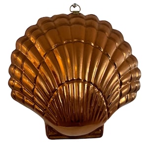 May include: A copper-colored, shell-shaped mold with a decorative hanging loop. The mold features a detailed, ridged design, creating a textured surface. The item is likely used for baking or decorative purposes.