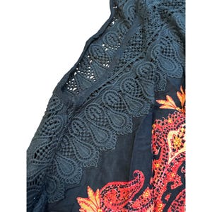 May include: Dark blue top with intricate lace detailing along the sleeves and neckline. The top features a vibrant paisley pattern in shades of red, orange, and yellow. The lace adds a delicate contrast to the bold print.