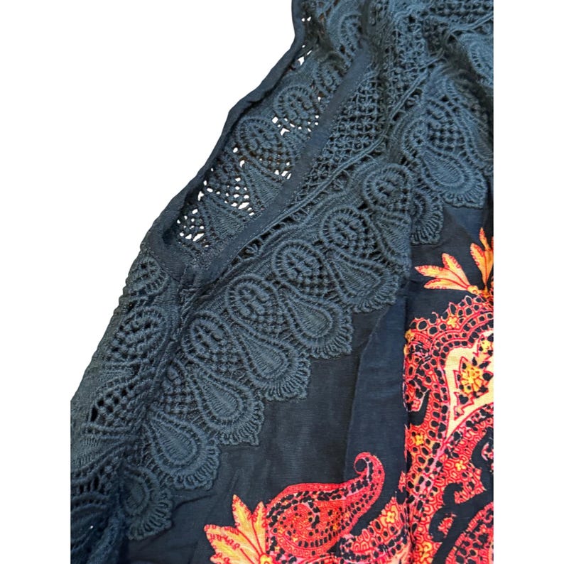 May include: Dark blue top with intricate lace detailing along the sleeves and neckline. The top features a vibrant paisley pattern in shades of red, orange, and yellow. The lace adds a delicate contrast to the bold print.