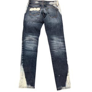 May include: Dark wash denim jeans with a faded design and white accents along the sides. The back pockets feature a decorative white design. The jeans have a classic five-pocket design and a button and zipper closure.