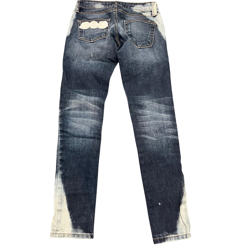 May include: Dark wash denim jeans with a faded design and white accents along the sides. The back pockets feature a decorative white design. The jeans have a classic five-pocket design and a button and zipper closure.