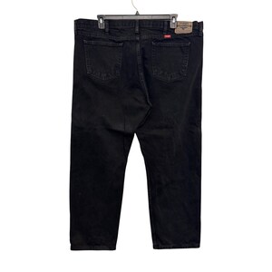 Op de afbeelding: Zwarte denim jeans met een klassiek ontwerp met vijf zakken. De jeans hangen aan een zwarte hanger. Het Wrangler-merklabel is zichtbaar op de achterzak. De jeans lijken maat 48 te hebben.
