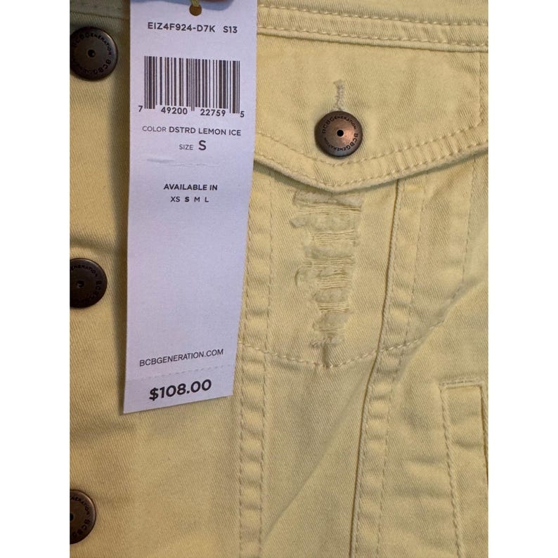 May include: Close-up of a pale yellow denim jacket with distressed details. The jacket has a button closure and a small pocket. A tag displays the colour "DSTRD LEMON ICE" and size "S". The brand name "BCBGENERATION" is visible.