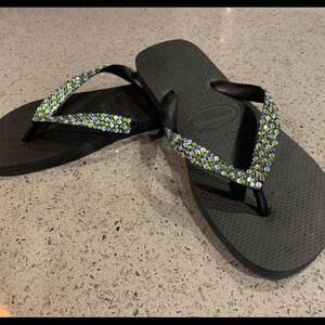 May include: A pair of black flip-flops with green and blue rhinestones on the straps.