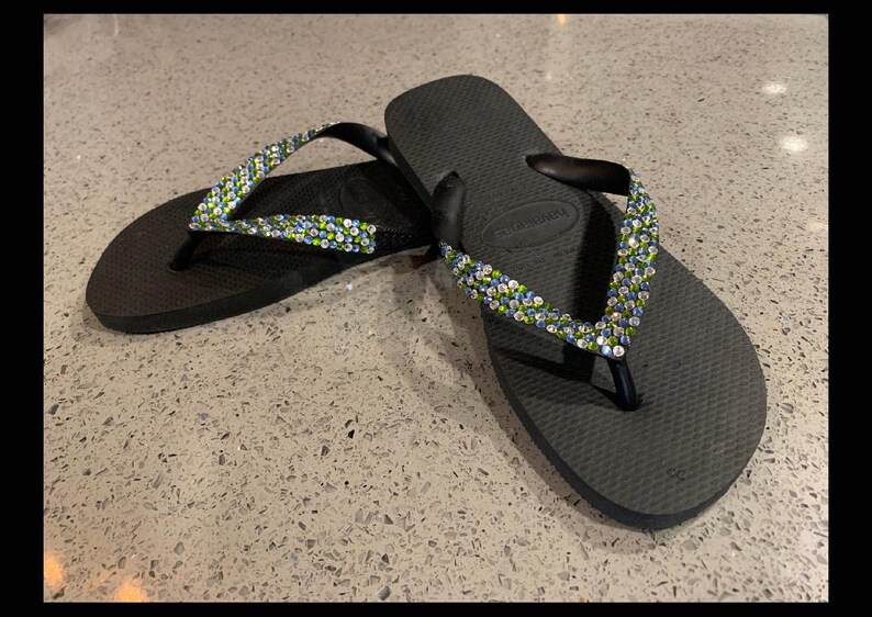 May include: A pair of black flip-flops with green and blue rhinestones on the straps.