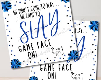 May include: Two white signs with black text and blue and black pom-poms. The text on the signs reads "We didn't come to play... We came to slay. Game face on!"
