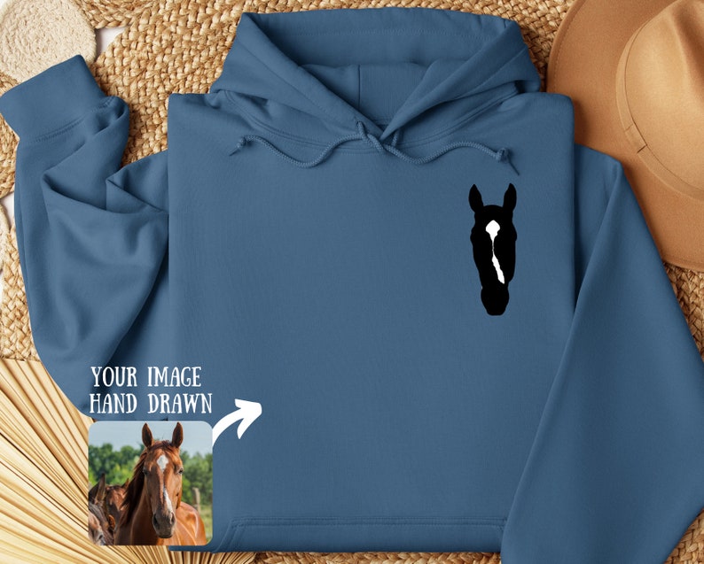 May include: A blue hooded sweatshirt with a black silhouette of a horse's head on the front. The text "YOUR IMAGE HAND DRAWN" is on the left side of the sweatshirt with an arrow pointing to a small image of a brown horse's head.