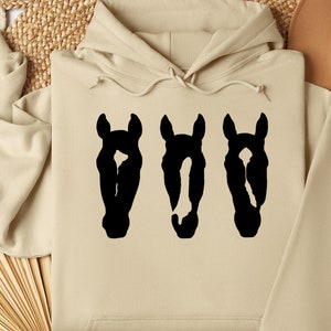 May include: A beige hoodie with a black silhouette of three horse heads printed on the front.