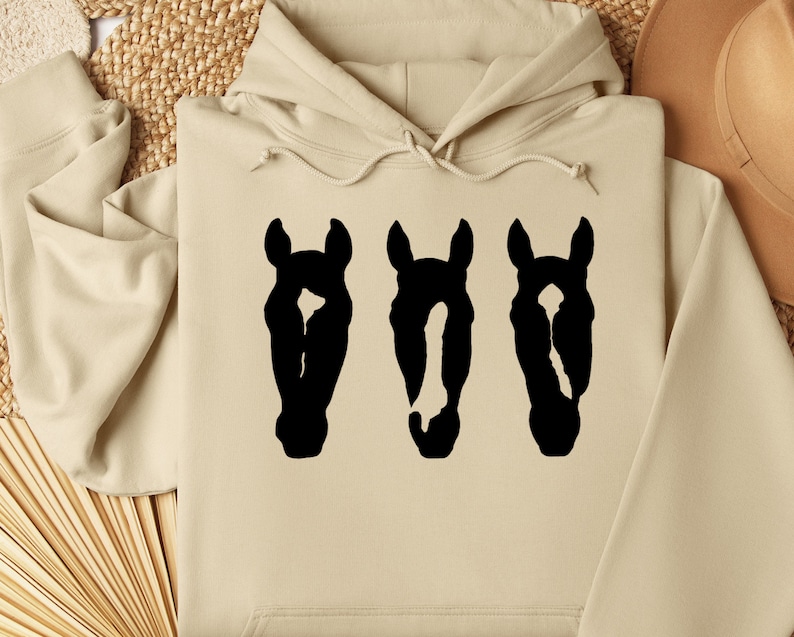May include: A beige hoodie with a black silhouette of three horse heads printed on the front.