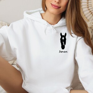 May include: White hooded sweatshirt with a black silhouette of a horse's head and the name "Samson" printed on the front.