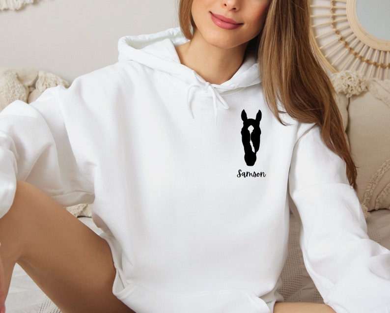 May include: White hooded sweatshirt with a black silhouette of a horse's head and the name "Samson" printed on the front.
