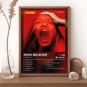 May include: A framed poster featuring the Scorpions Rock Believer album cover with a red-toned portrait of a person with an open mouth. The text includes the band name, album title, year 2022, a tracklist of eleven songs, and a Spotify code.