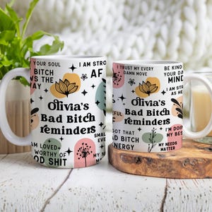 May include: Two white ceramic mugs with the text "Olivia's Bad Bitch Reminders" in black script. The mugs feature floral and star designs in pastel colors. One mug has the text "Your Soul Bitch Wins the Day".