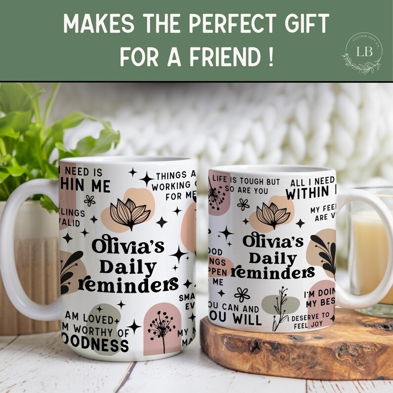 May include: Two white ceramic mugs with the text "Olivia's Daily Reminders" and inspirational phrases. The mugs feature floral and geometric designs in black, peach, and beige. The top of the image reads "MAKES THE PERFECT GIFT FOR A FRIEND!"