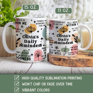 May include: Two white ceramic mugs with the text "Olivia's Daily Reminders" and various inspirational phrases. The mugs have floral and abstract designs in pastel colors. One mug is 15 oz, the other is 11 oz.