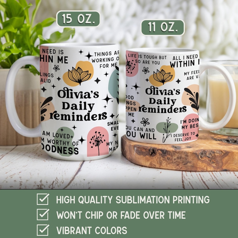 May include: Two white ceramic mugs with the text "Olivia's Daily Reminders" and various inspirational phrases. The mugs have floral and abstract designs in pastel colors. One mug is 15 oz, the other is 11 oz.