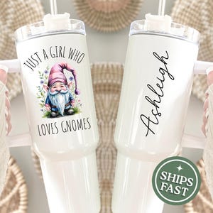 May include: White insulated tumbler with a handle, featuring a watercolor gnome illustration and the text "JUST A GIRL WHO LOVES GNOMES." The other side has the name "Ashleigh" in script. A green circle with "SHIPS FAST" is also visible.