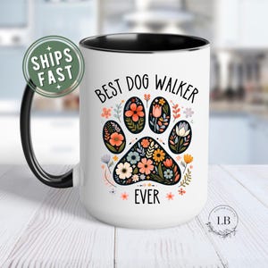 May include: White ceramic mug with a black handle and rim, featuring a floral paw print design. The words "BEST DOG WALKER EVER" are printed above and below the paw print. The mug has a glossy finish and is suitable for hot or cold beverages.